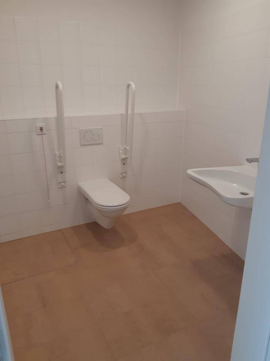Barrierefreie Toilette mit Haltegriffen, wandhängendem WC und einem Waschbecken.