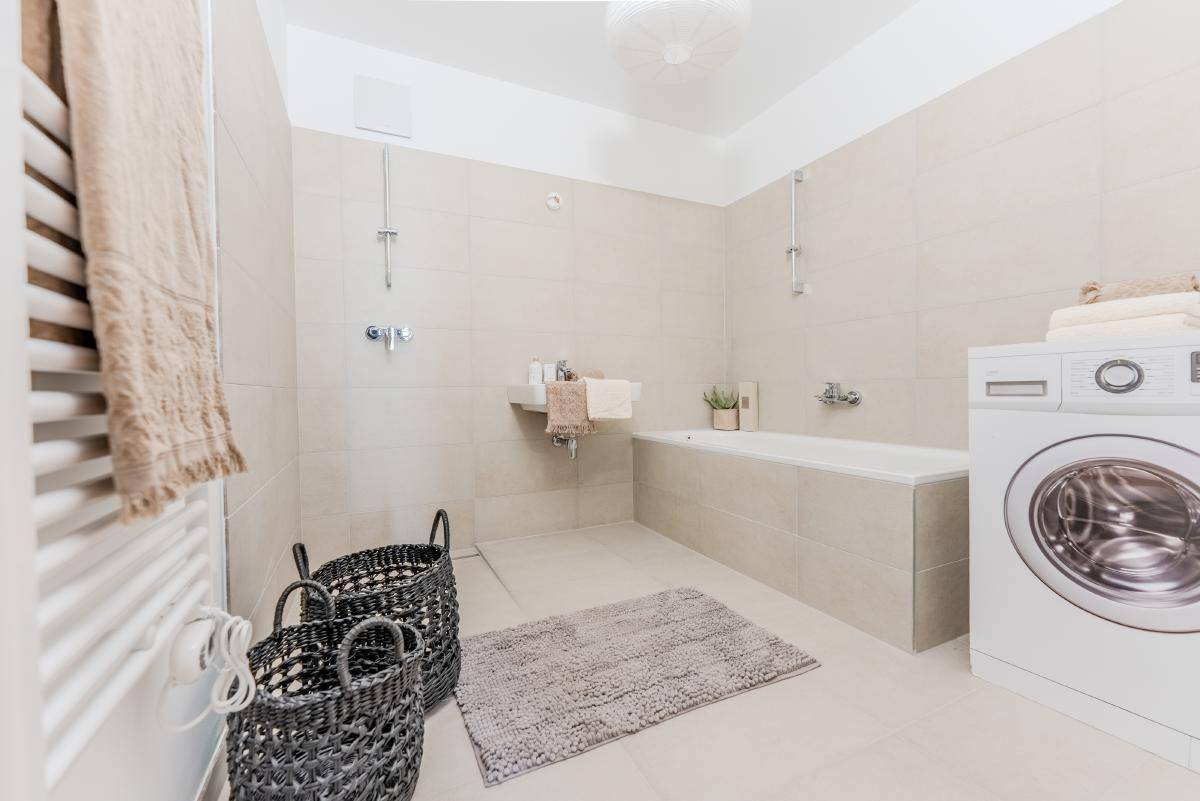 Funktionales Badezimmer mit Badewanne, integrierter Dusche und Waschmaschine, ausgestattet mit einem Handtuchheizkörper.