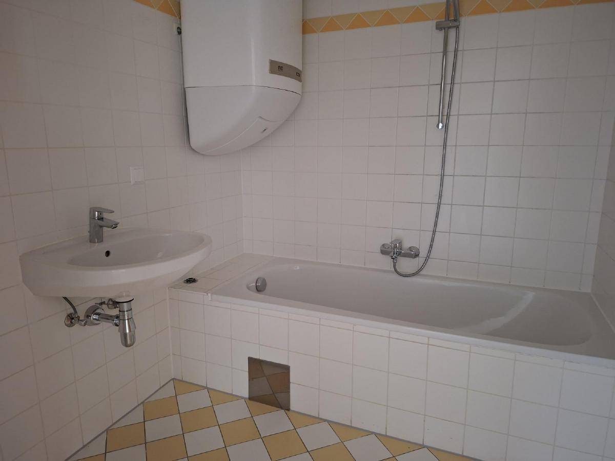 Badezimmer mit Badewanne, Waschbecken und gelb-weiß karierten Fliesenboden.