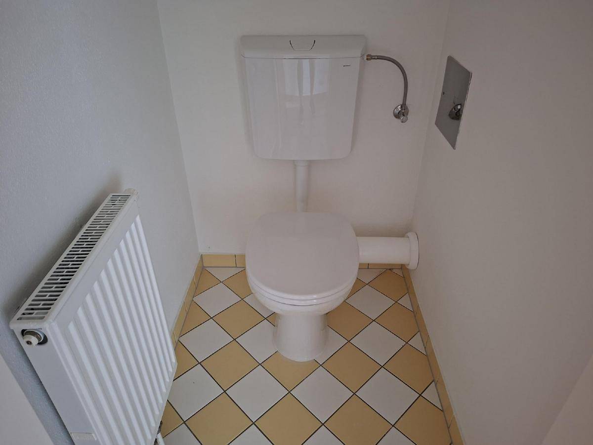 Kleines WC mit Toilette, Heizkörper und gelb-weiß karierten Fliesenboden.