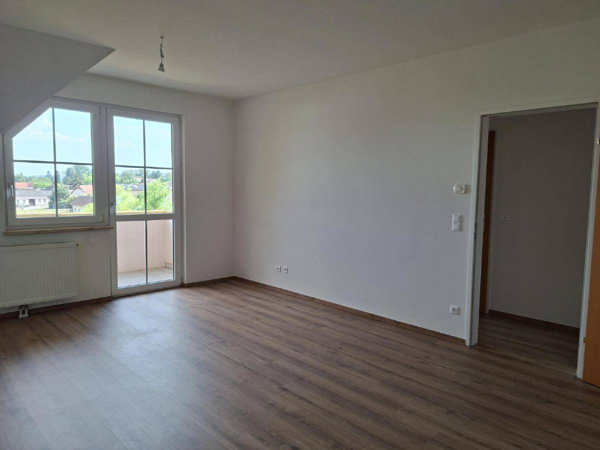 Heller Wohnraum mit Laminatboden, weißen Wänden und Zugang zu einem kleinen Balkon.