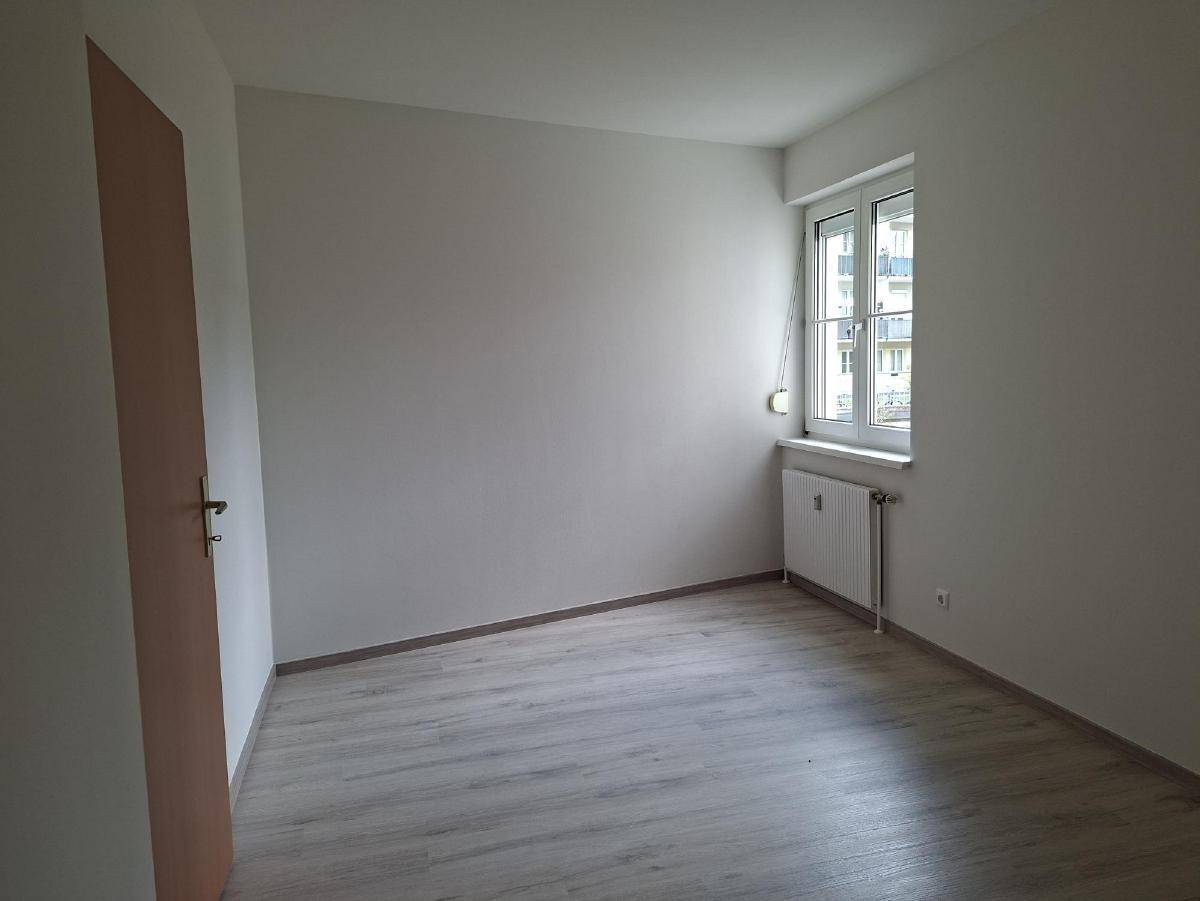Leeres Schlafzimmer mit Laminatboden, einem Fenster und einem Heizkörper unter dem Fenster.