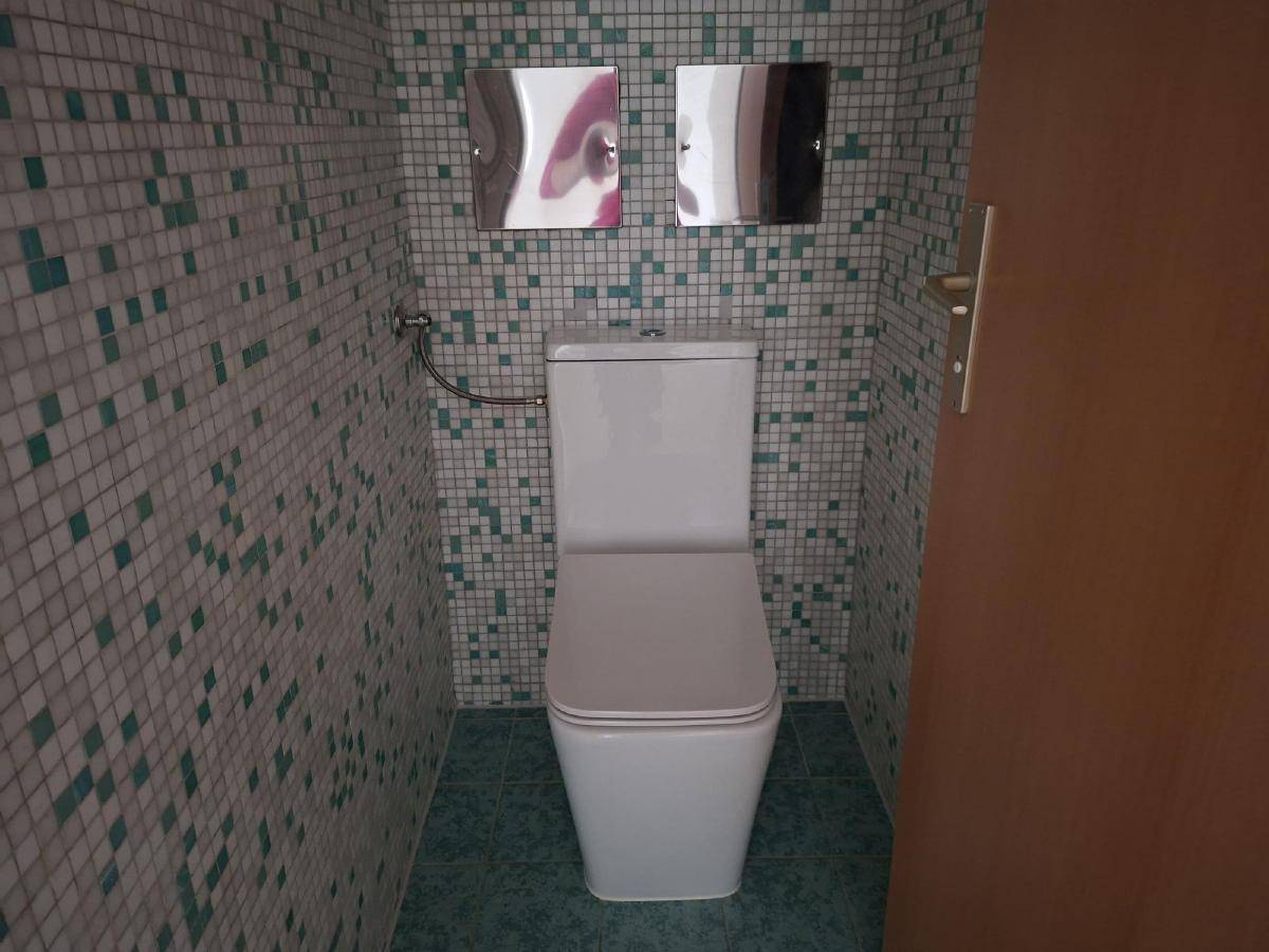 Separate Toilette mit Mosaikfliesen an den Wänden und einem modernen WC.
