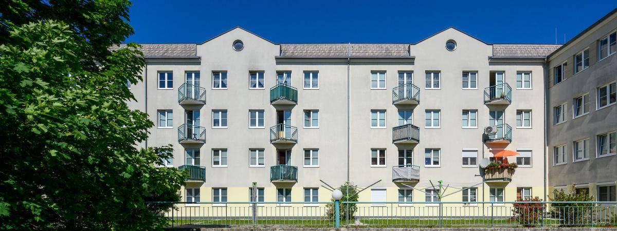Fassade eines Wohngebäudes mit vielen Fenstern und kleinen Balkonen unter strahlend blauem Himmel.