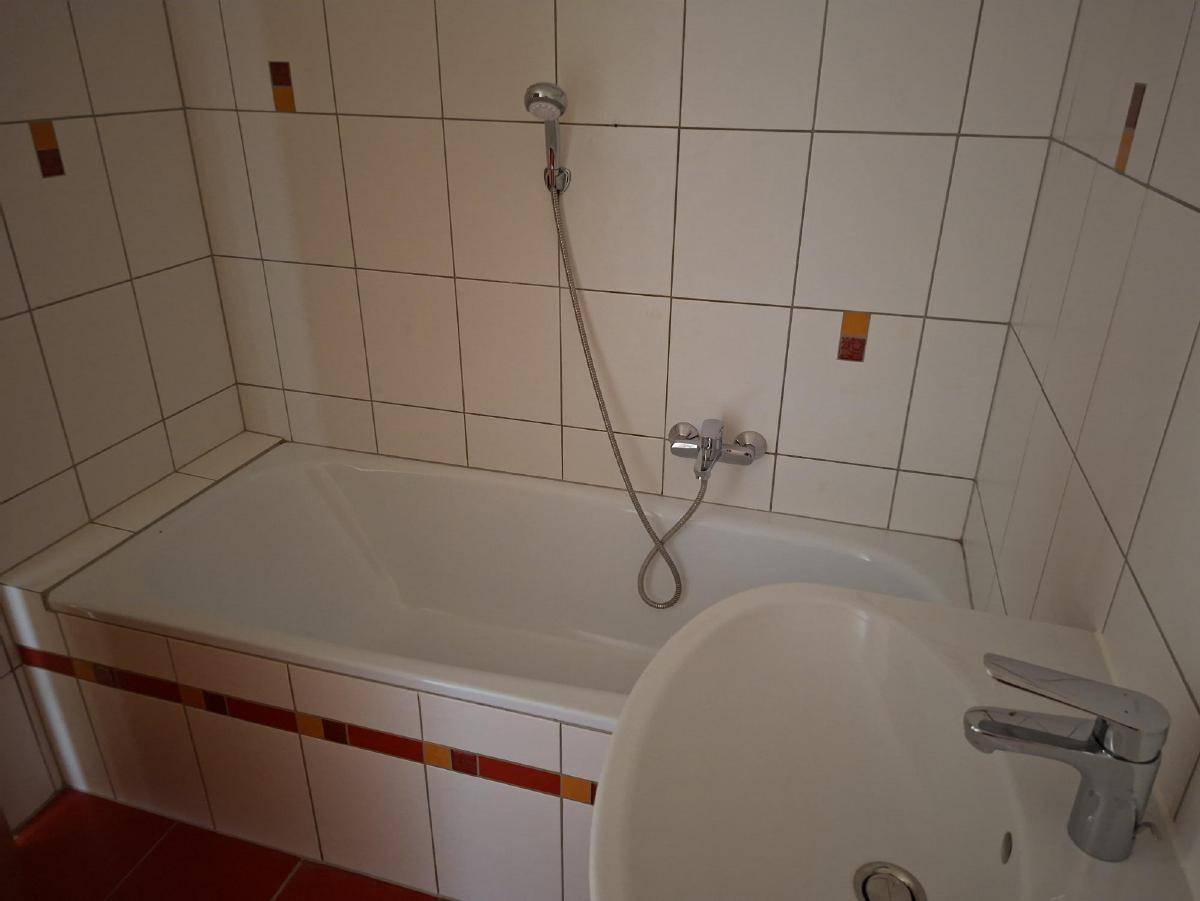Badezimmer mit Badewanne, Waschbecken und weißen Fliesen mit farbigen Akzenten.