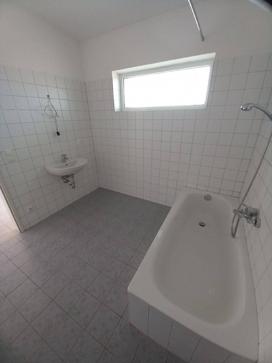 Badezimmer mit Badewanne, Waschbecken und Fliesen an Wänden und Boden, inklusive Fenster.