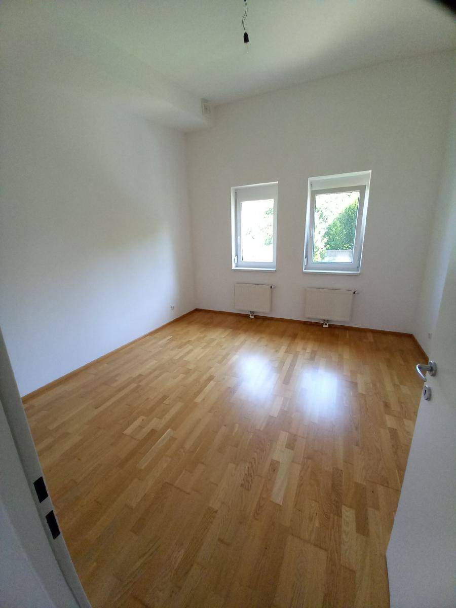 Leeres Schlafzimmer mit Parkettboden und zwei Fenstern für viel Tageslicht.