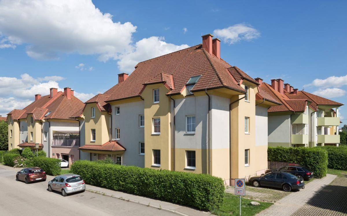 Wohngebäude mit Satteldach, Balkonen und Parkplätzen entlang einer ruhigen Straße.