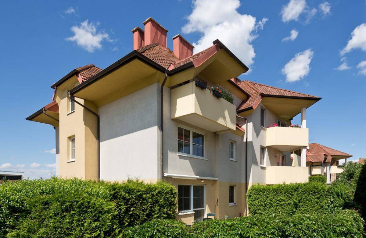 Detailansicht eines Wohnhauses mit Balkonen, Fenstern und umgebenden Hecken unter klarem Himmel.