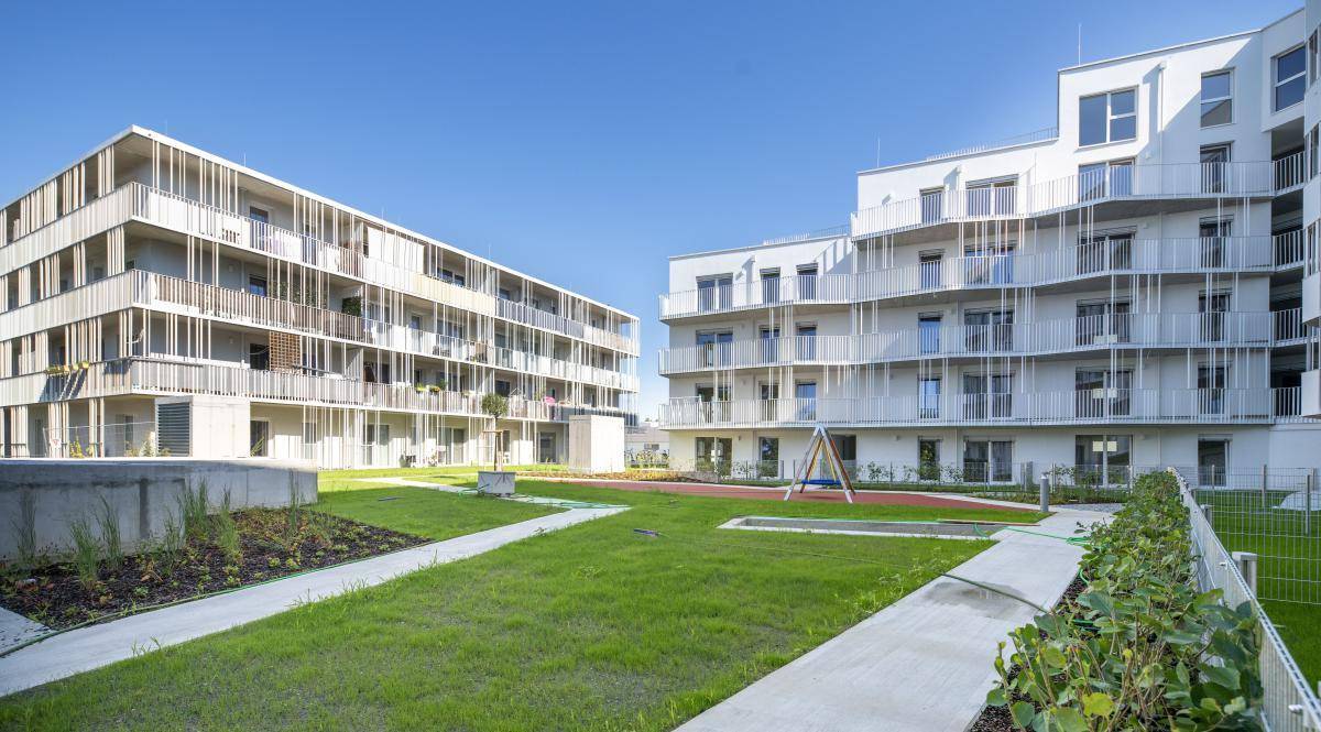 Zwei moderne Wohngebäude mit gepflegter Grünfläche und kleinem Spielbereich im Freien.