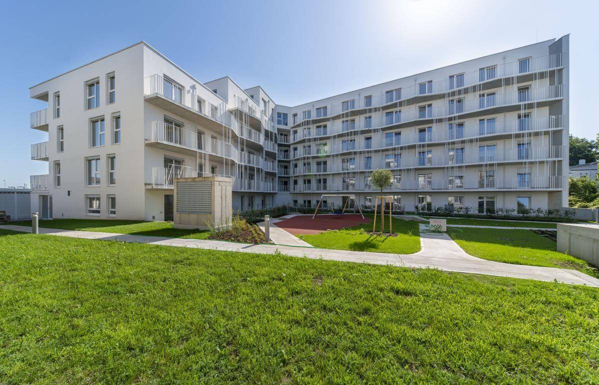 Modernes Wohngebäude mit weißer Fassade, umgeben von Grünflächen und einem Spielplatz.