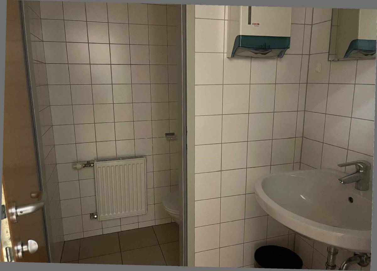 Gefliestes Badezimmer mit Waschbecken und einem Duschbereich, ausgestattet mit Standardarmaturen.