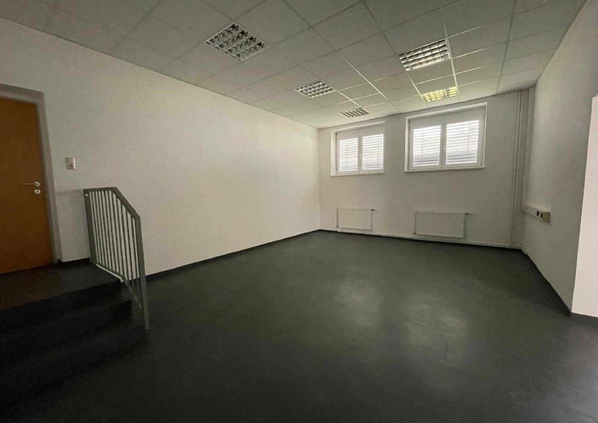 Heller Gewerberaum mit dunklem Boden, weißen Wänden und einem Treppenaufgang auf der linken Seite.
