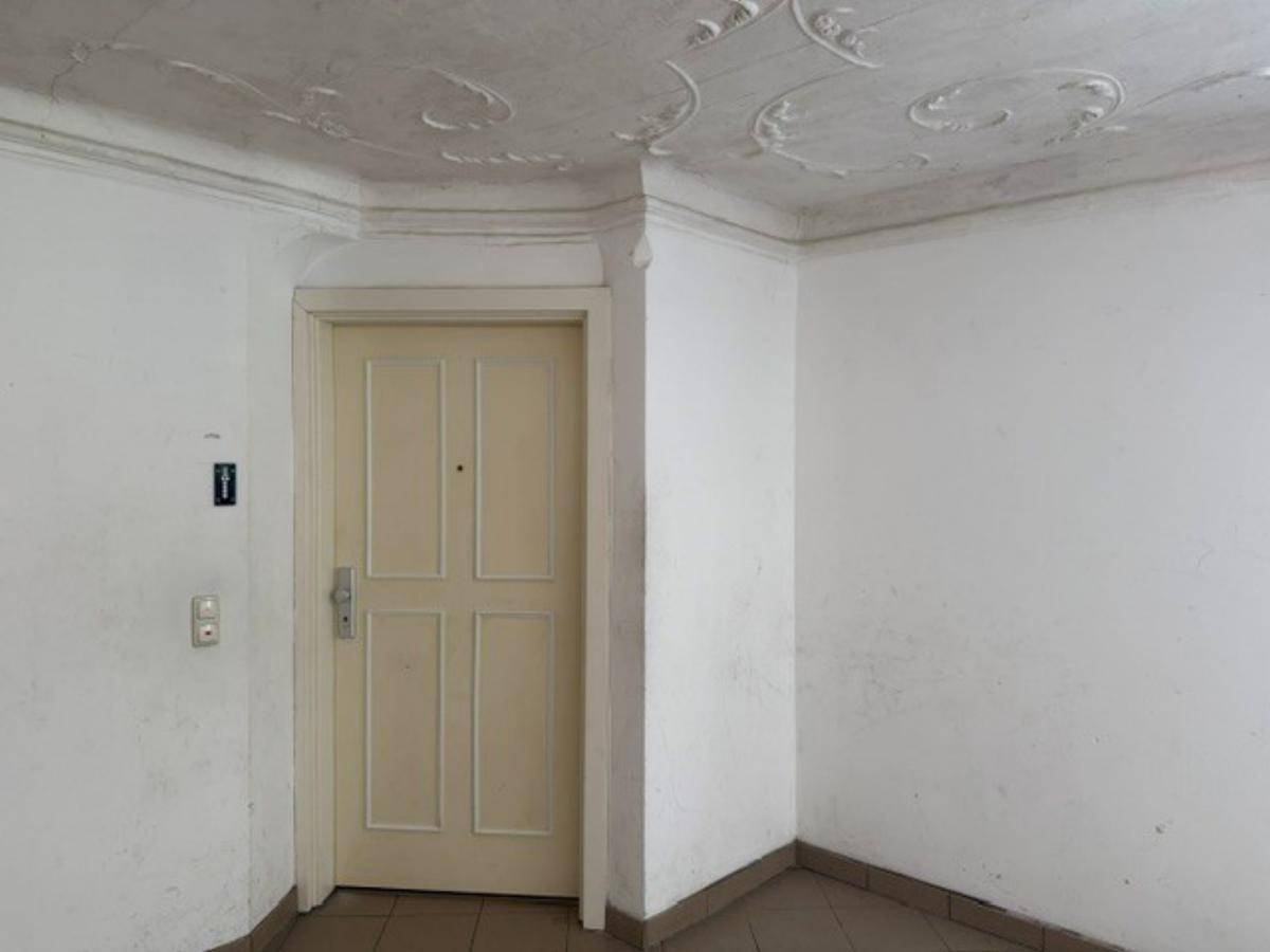 Eingangsbereich mit einer Holztür, Fliesenboden und einer Stuckdecke mit Ornamenten.
