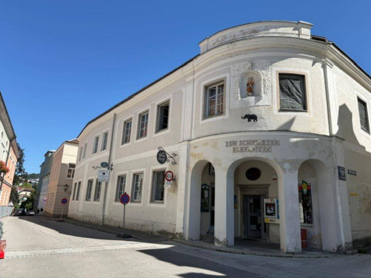 Historisches Gebäude mit abgerundeter Ecke und Arkaden im Erdgeschoss an einer Straße.