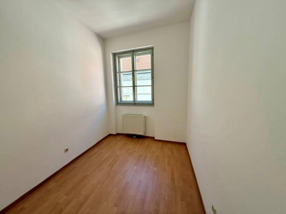 Kleines, helles Zimmer mit Laminatboden, weißen Wänden und einem Fenster zur Straße.