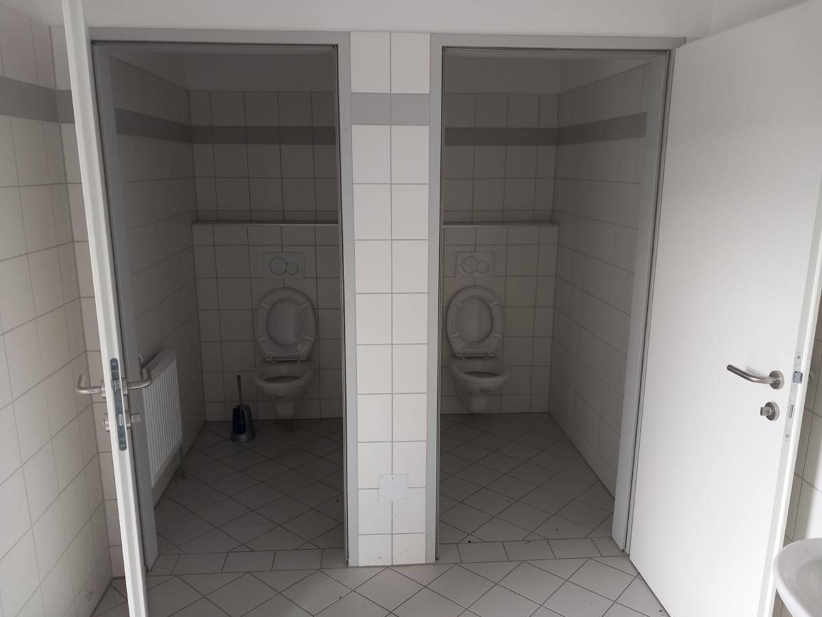 Zwei separate Toilettenkabinen mit weißen Fliesen an Wänden und Boden sowie wandhängenden Toiletten.