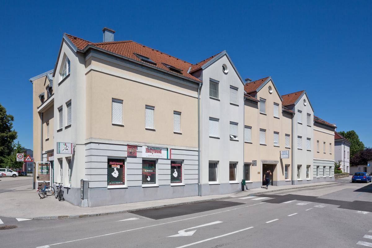 Lange Fassade eines Gebäudes mit Geschäften und Wohnungen entlang einer ruhigen Straße.