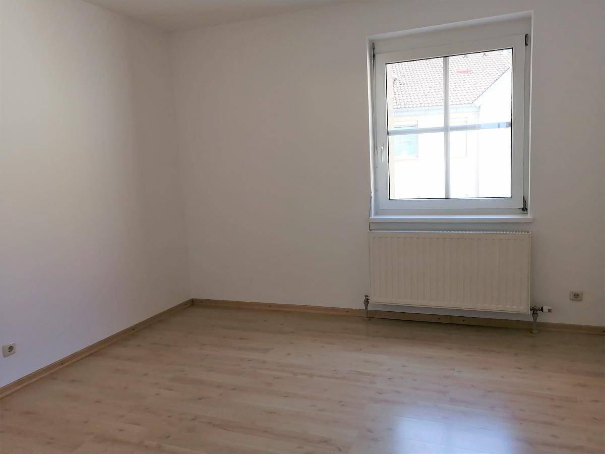Leerer Raum mit Laminatboden, einem Fenster und Heizkörper, ideal für Schlaf- oder Wohnbereich.