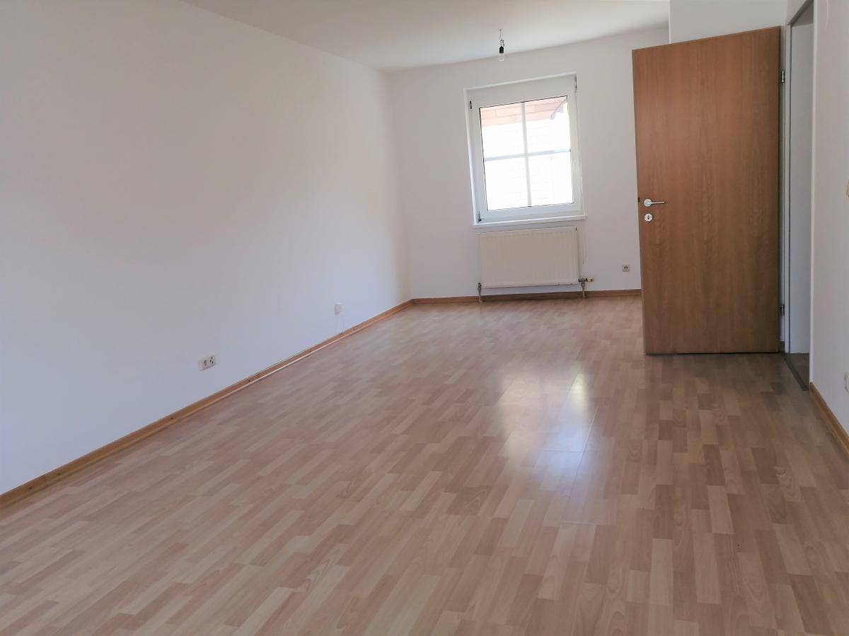 Heller, leerer Raum mit Laminatboden und einem Fenster, bereit zur individuellen Gestaltung.