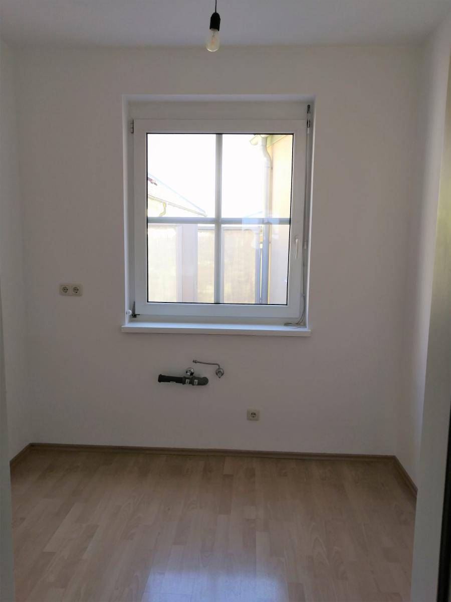 Kleiner Raum mit Laminatboden, Fenster und Anschlüssen für eine zukünftige Küche oder Hauswirtschaftsraum.