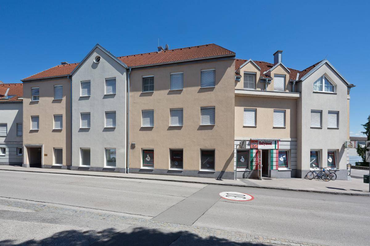 Gebäudekomplex mit Geschäften im Erdgeschoss und Wohnungen darüber an einer städtischen Straße.