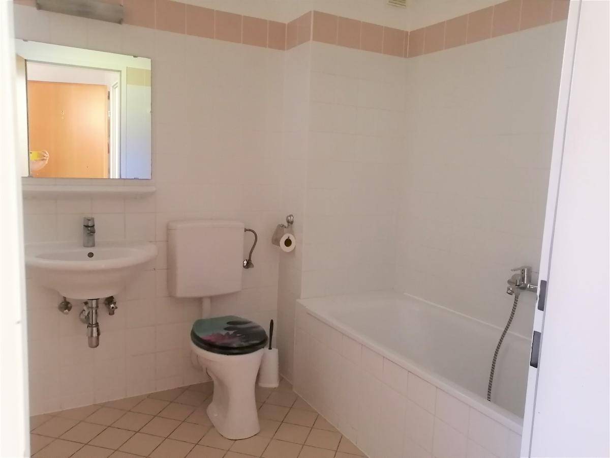 Badezimmer mit Badewanne, WC, Waschbecken und hellen Fliesen in einem gepflegten Zustand.