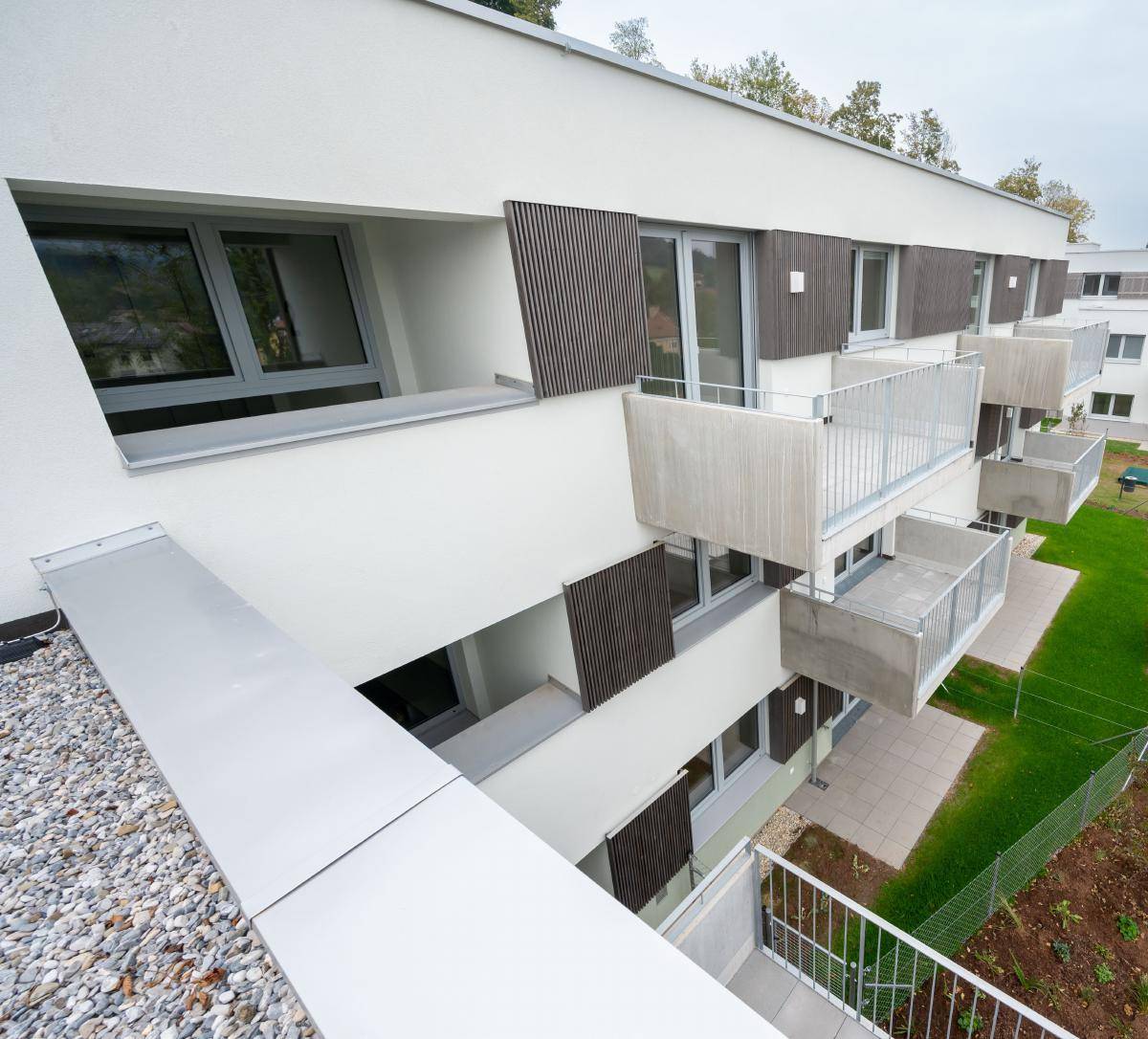 Ansicht eines modernen Wohnkomplexes mit gestaffelten Balkonen und großen Fenstern, umgeben von Grün.