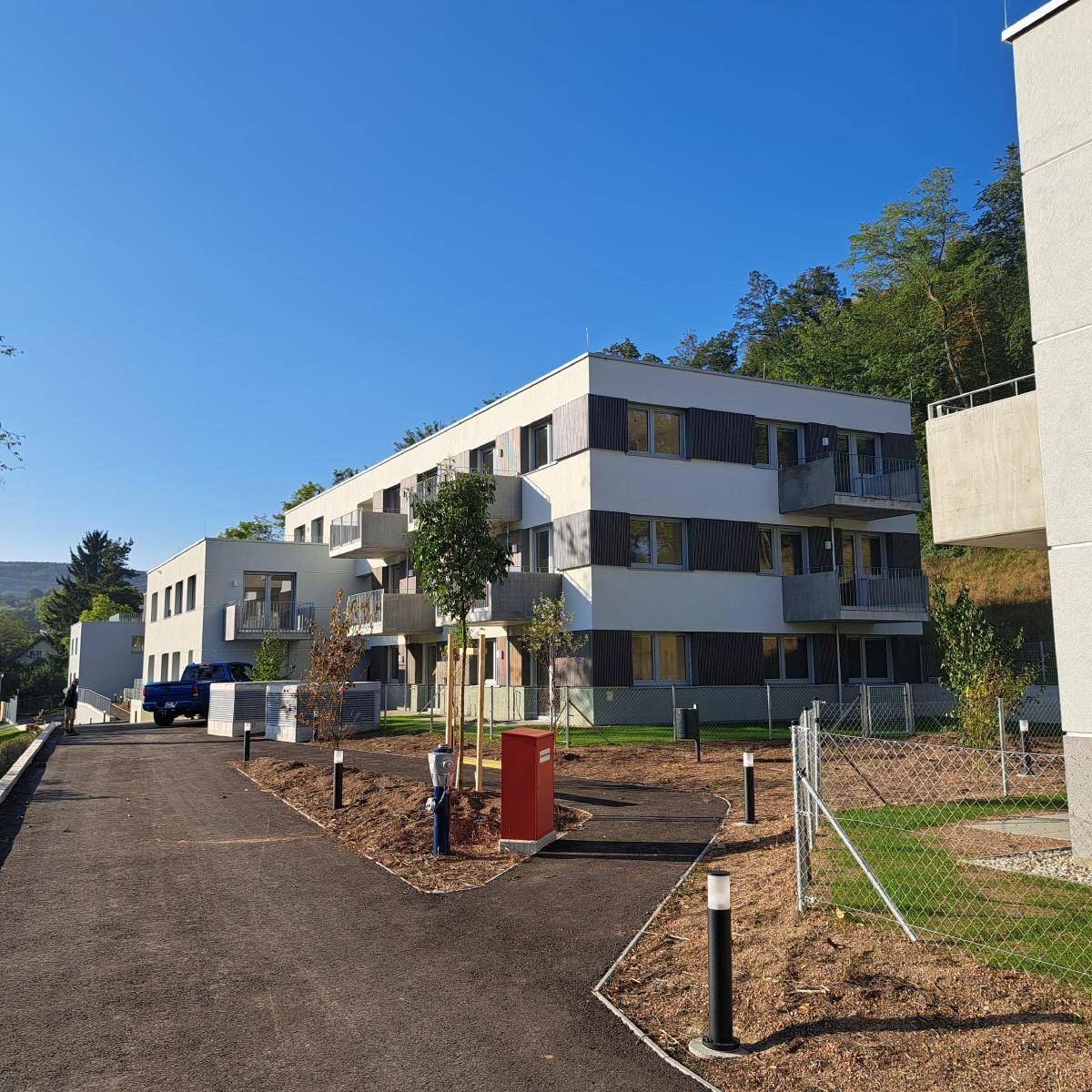 Mehrere moderne Wohngebäude mit hellen Fassaden und Holzdetails, umgeben von neu angelegten Grünflächen.