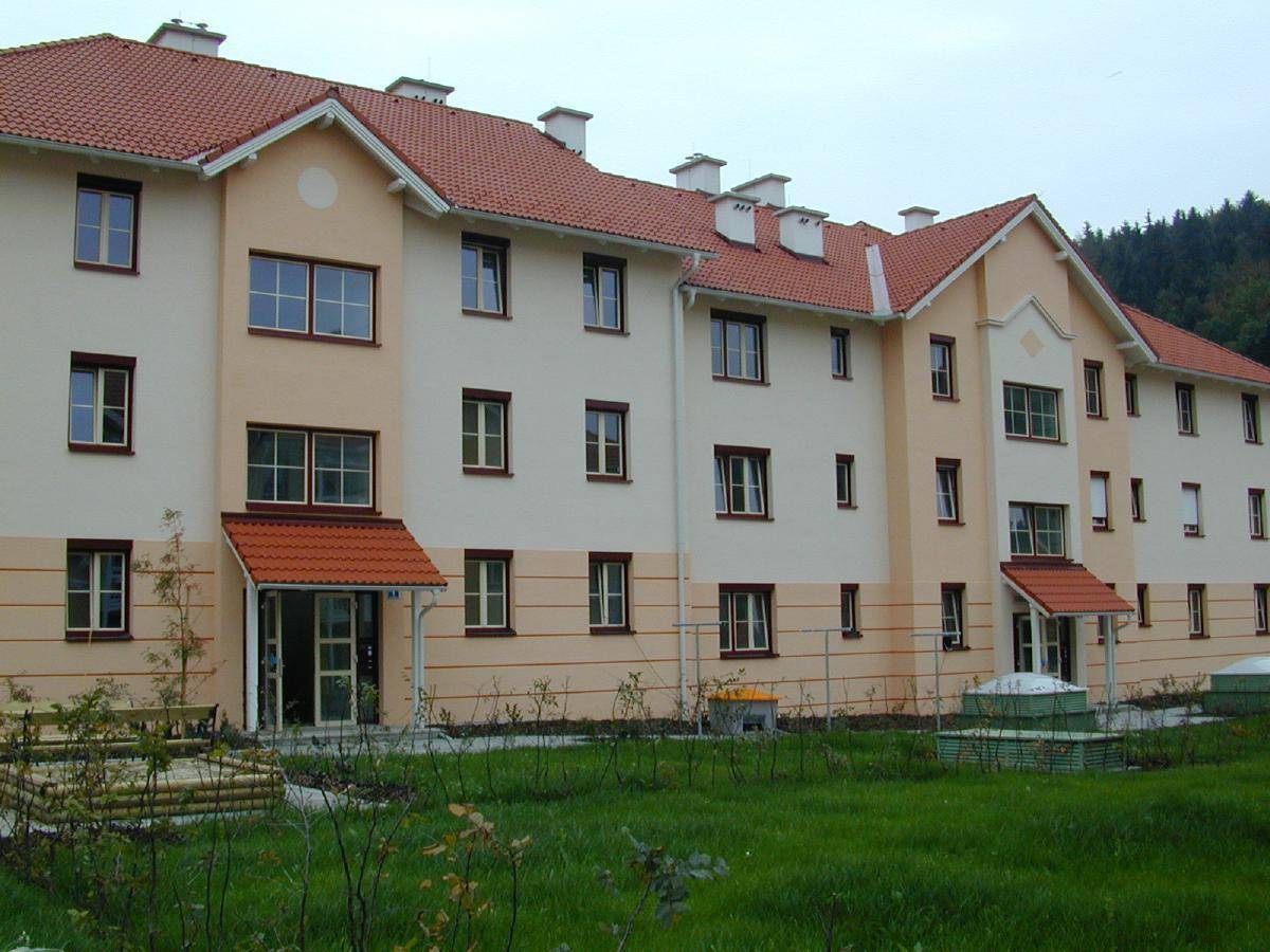 Wohngebäude mit beiger Fassade, roten Ziegeldächern und mehreren Eingängen, umgeben von Rasenflächen.