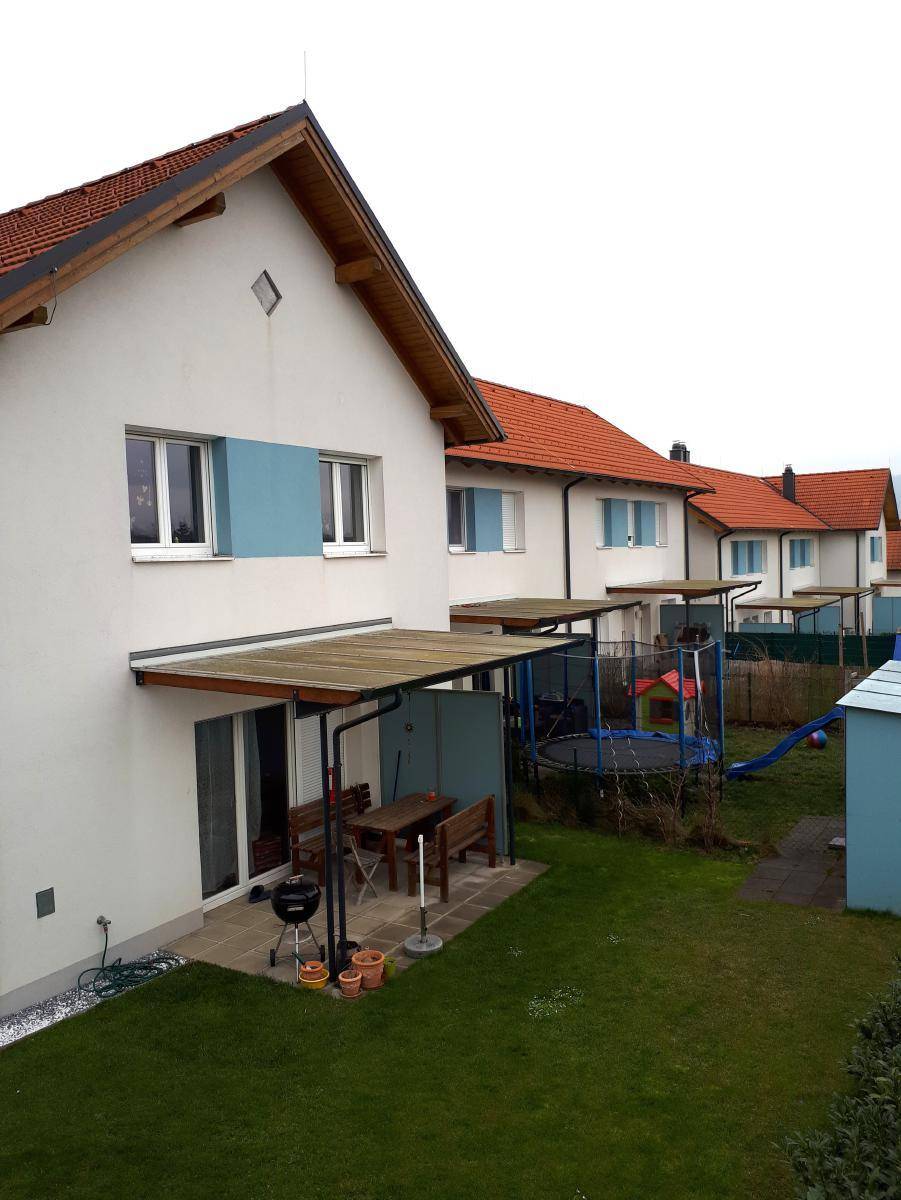 Hinterhof eines Reihenhauses mit Terrasse, Gartenmöbeln, Rasenfläche und Kinderspielgeräten.