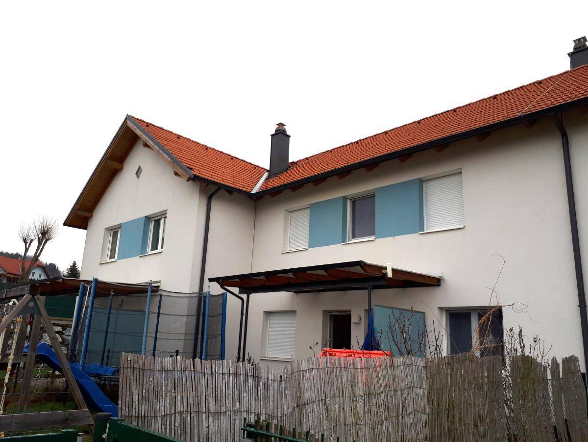 Rückseite eines Reihenhauses mit Garten, Trampolin und Rutsche, umgeben von einem Holzzaun.