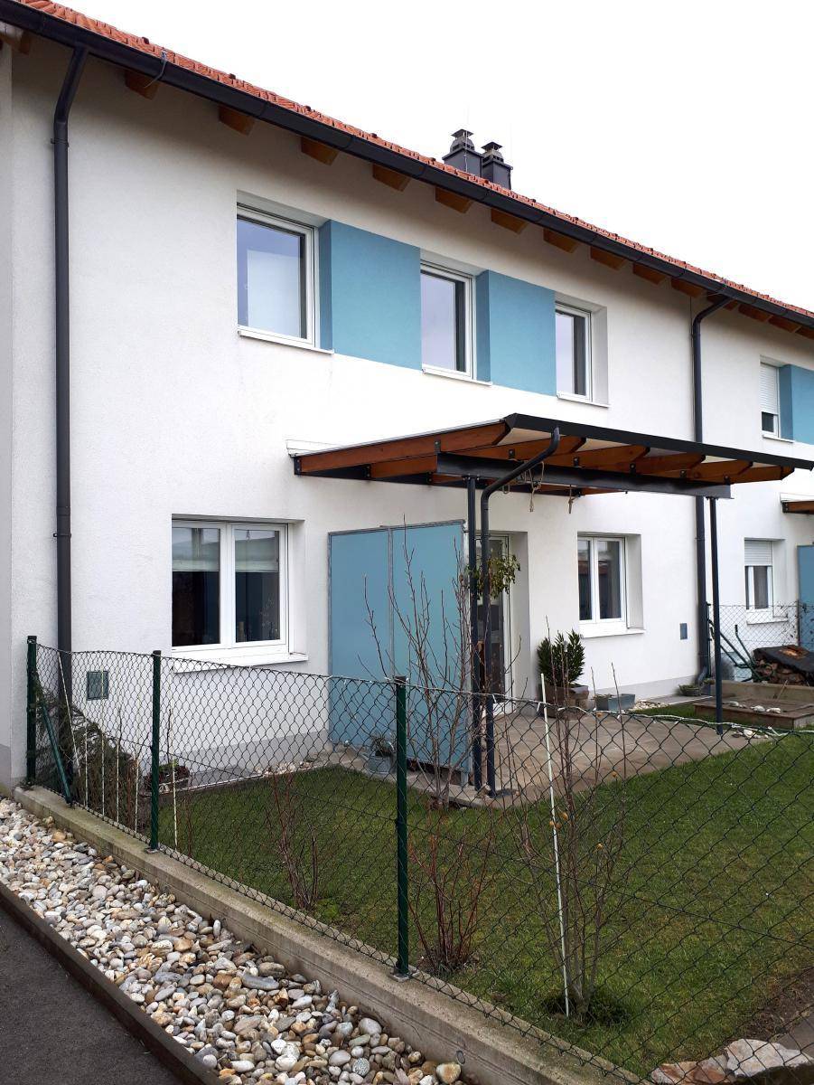 Vorderansicht eines Reihenhauses mit kleinem Vorgarten, Zaun und blauen Fassadenakzenten.