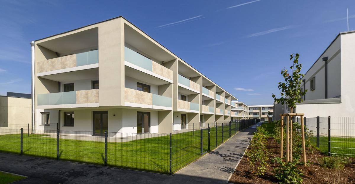 Lange Reihe moderner Wohngebäude mit Balkonen und großen Fenstern, umgeben von grünen Rasenflächen.