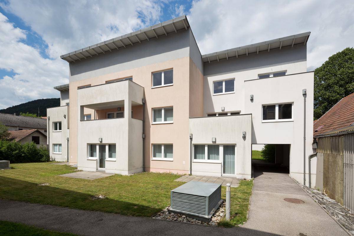 Ansicht des modernen Mehrfamilienhauses mit hellen Fassaden und Zufahrt zu den Parkplätzen.
