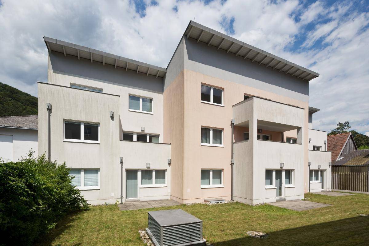 Rückansicht des modernen Wohngebäudes mit Balkonen und gepflegter Grünfläche im Außenbereich.