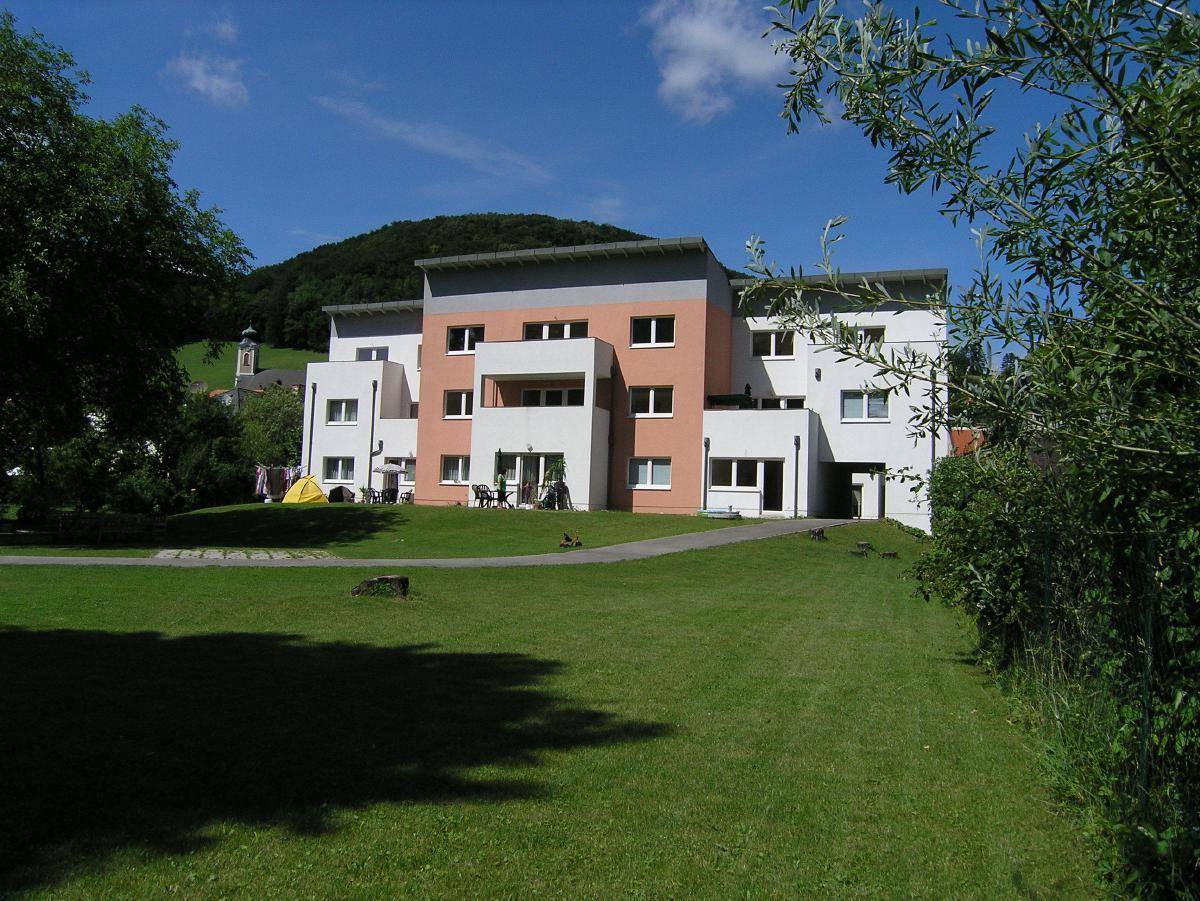 Weitläufige Außenansicht des Wohnhauses mit großem Rasen und Bergblick unter blauem Himmel.