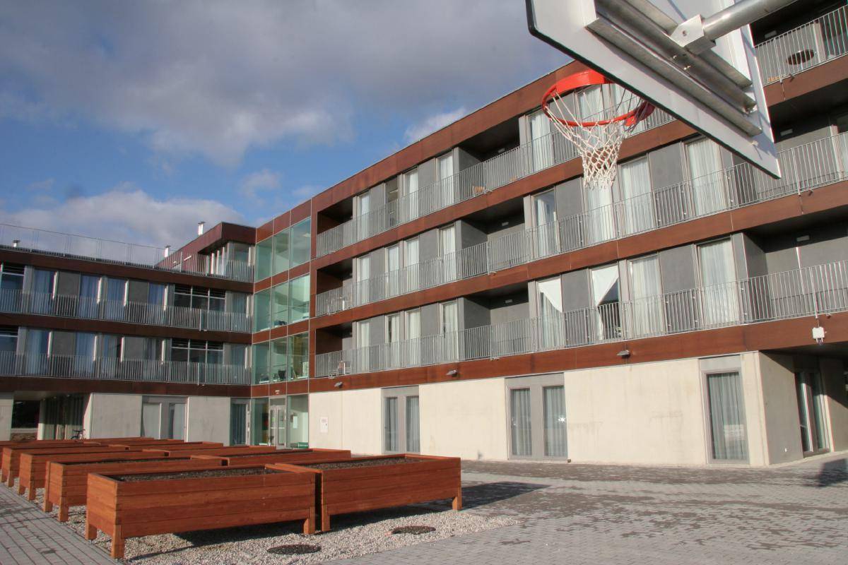 Innenhof eines modernen Wohnkomplexes mit Basketballkorb und Holzpflanzkübeln, umgeben von Balkonen.