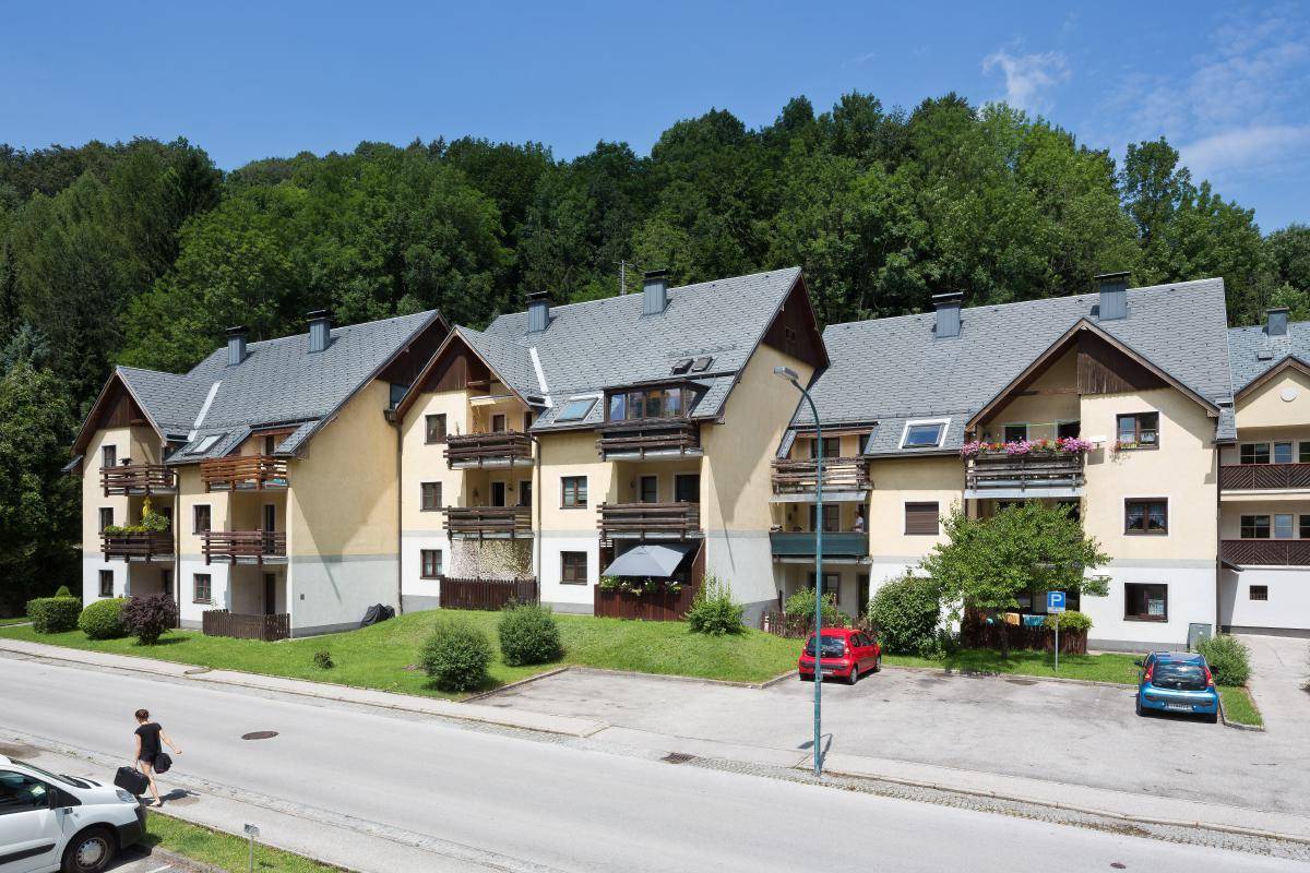 Mehrere Mehrfamilienhäuser mit Balkonen und Blick auf bewaldete Hügel und die Straße.