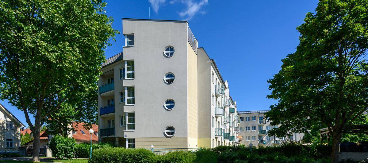 Seitenansicht eines modernen Wohngebäudes mit runden Fenstern und Balkonen, umgeben von Bäumen.