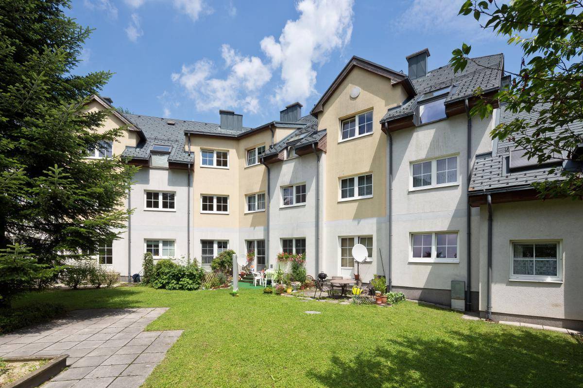 Rückansicht eines Mehrfamilienhauses mit gepflegtem Gemeinschaftsgarten und Sitzgelegenheiten im Freien.
