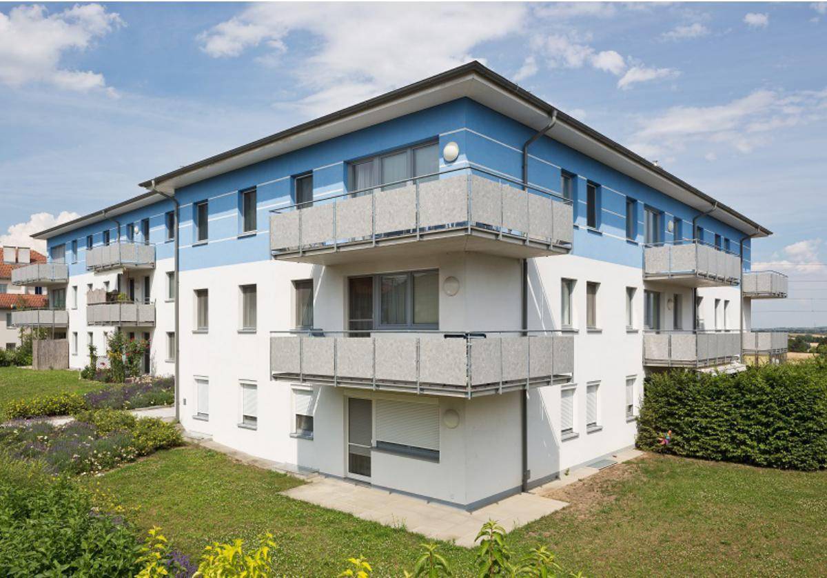 Wohngebäude mit blauer und weißer Fassade, mehreren Balkonen und umgebender Rasenfläche an einem sonnigen Tag.
