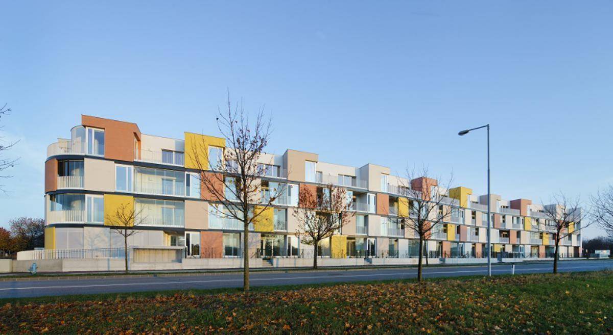Lange Fassade eines modernen Wohngebäudes mit farbigen Akzenten und Balkonen an einem Herbsttag.