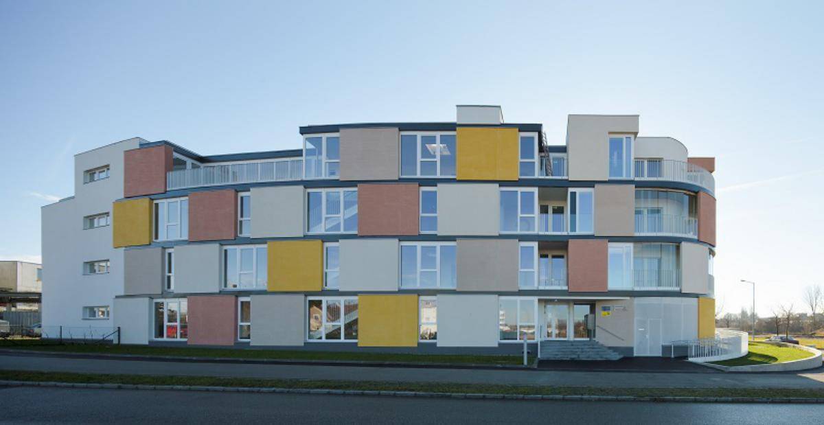 Geschwungene Fassade eines modernen Wohnkomplexes mit großen Fenstern und farbigen Paneelen.