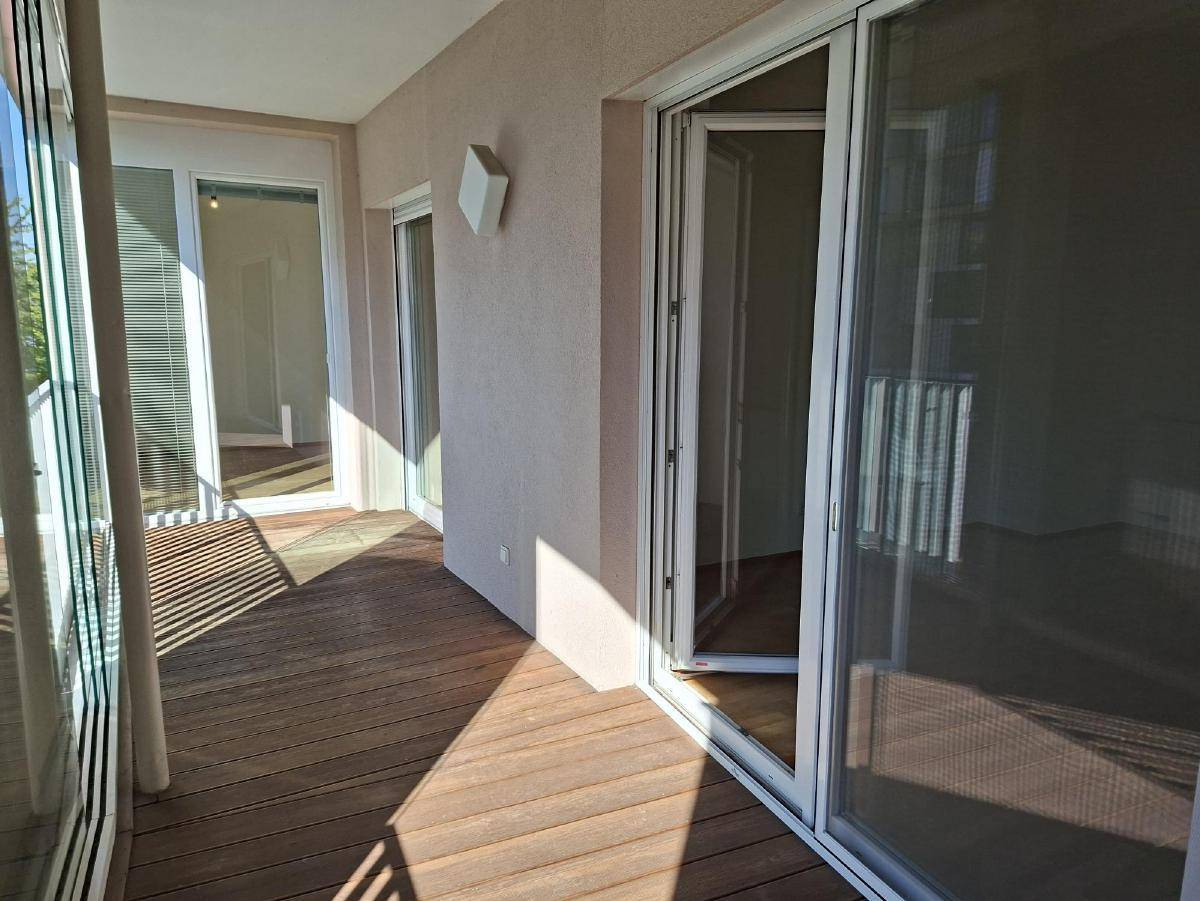 Geräumiger Balkon mit Holzdielenboden und viel Sonnenlicht, zugänglich von mehreren Räumen.