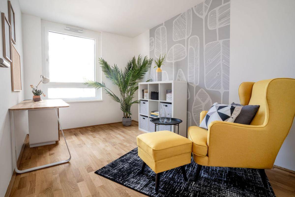 Helles Arbeitszimmer mit modernem gelbem Sessel, Schreibtisch und dekorativer Tapete.