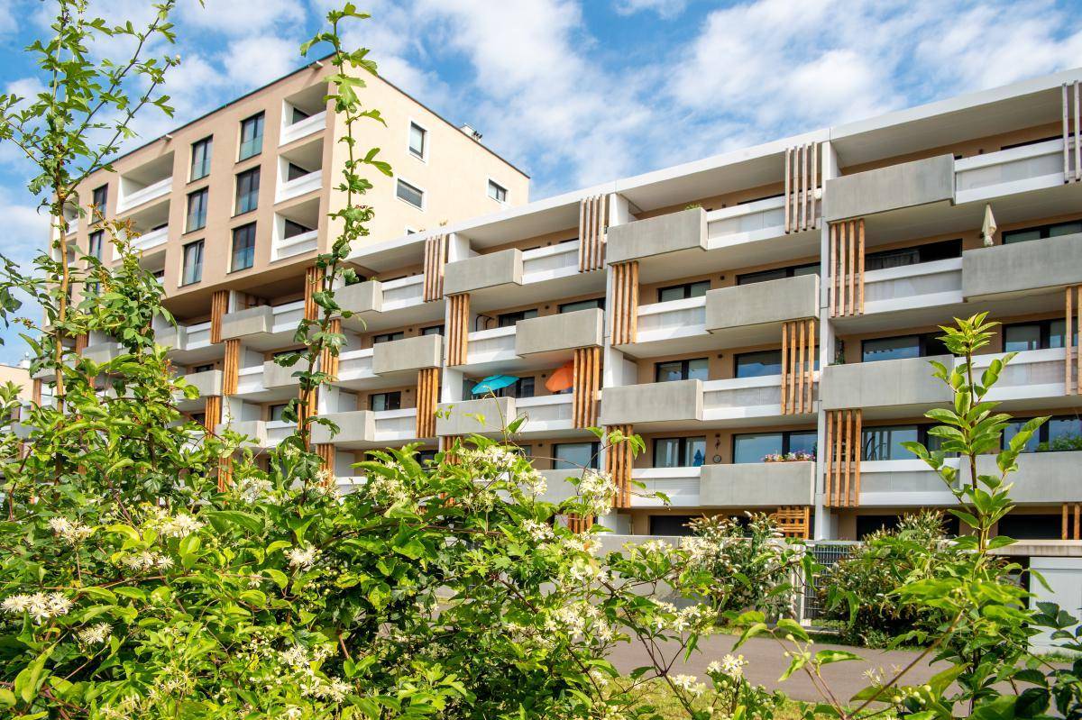 Mehrere moderne Wohngebäude mit Balkonen, umgeben von üppiger grüner Bepflanzung.