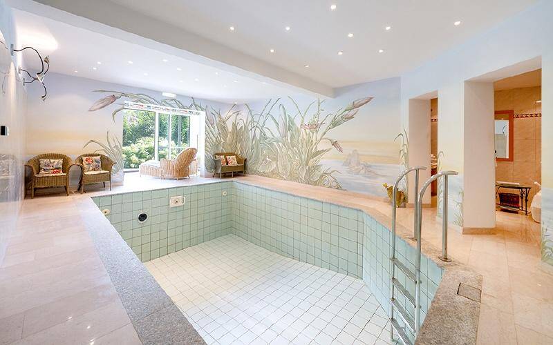 Heller Innenpoolbereich mit Wandmalereien, Liegestühlen und Zugang zum Garten.
