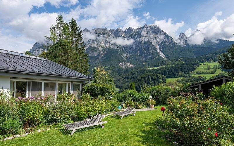 Gepflegter Garten mit Liegestühlen, umgeben von üppigem Grün und beeindruckendem Bergpanorama.