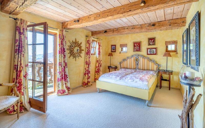 Farbenfrohes Schlafzimmer mit Holzbalkendecke, Teppichboden und Zugang zum Balkon.